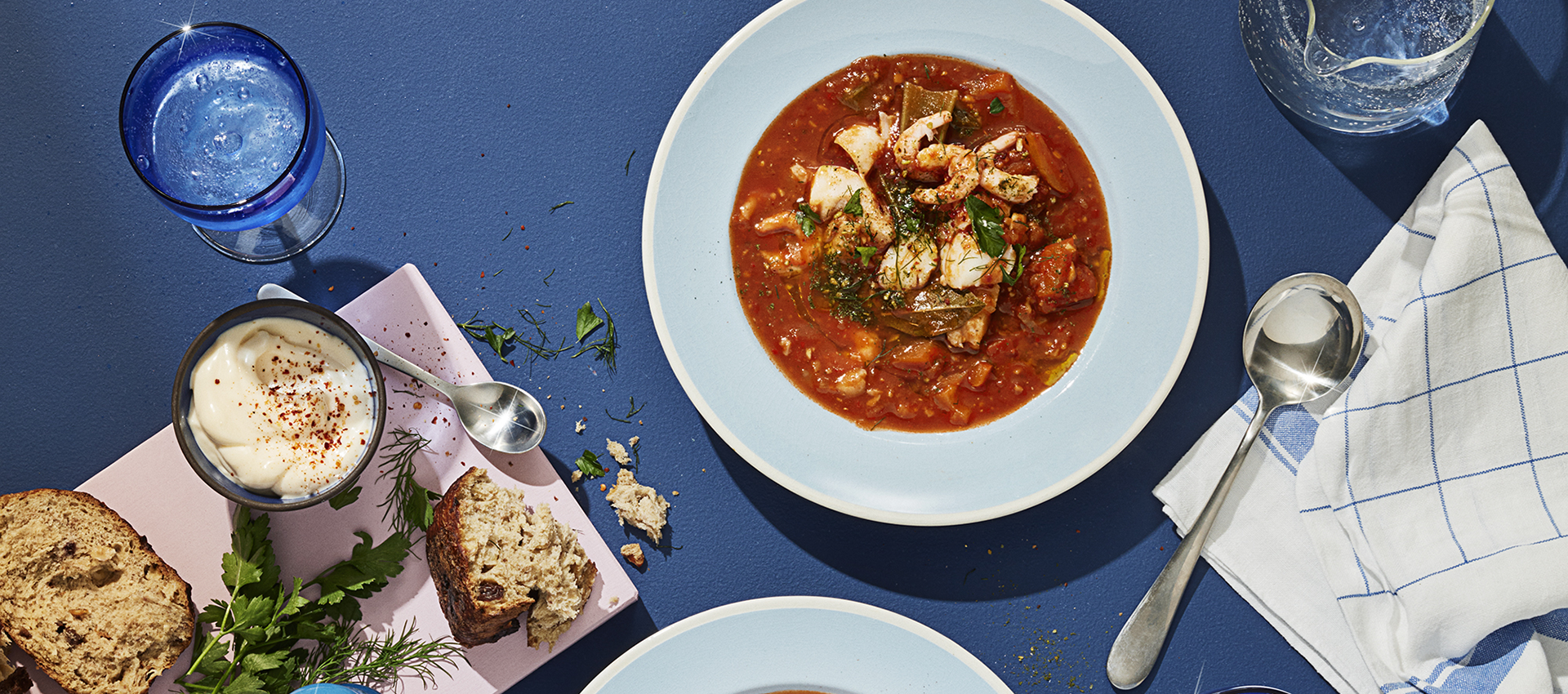  Fiskesuppe serveret på bord med brød, vand og tilbehør