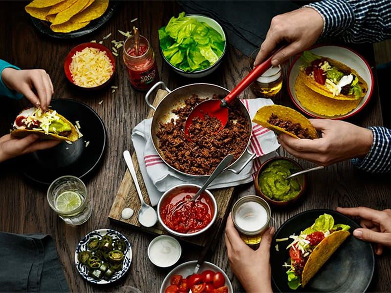 Bord uppdukat med tex mex mat och händer som plockar mat