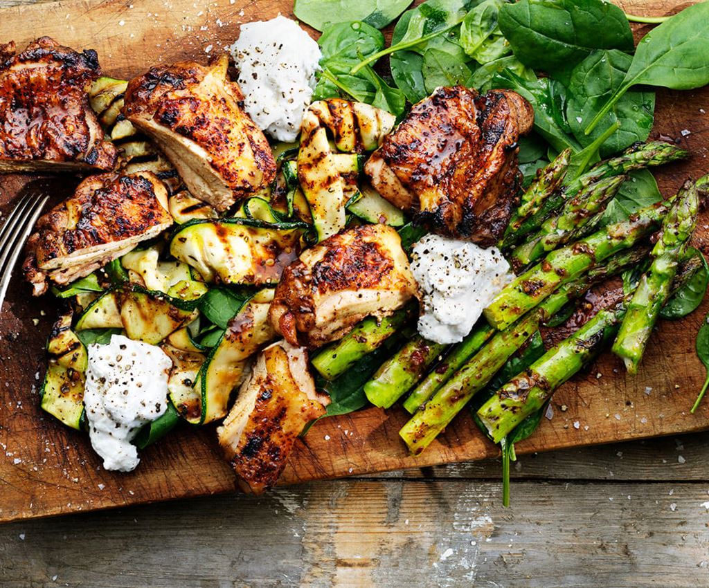 Grilled chicken and veggies plated on a wooden cutting board.