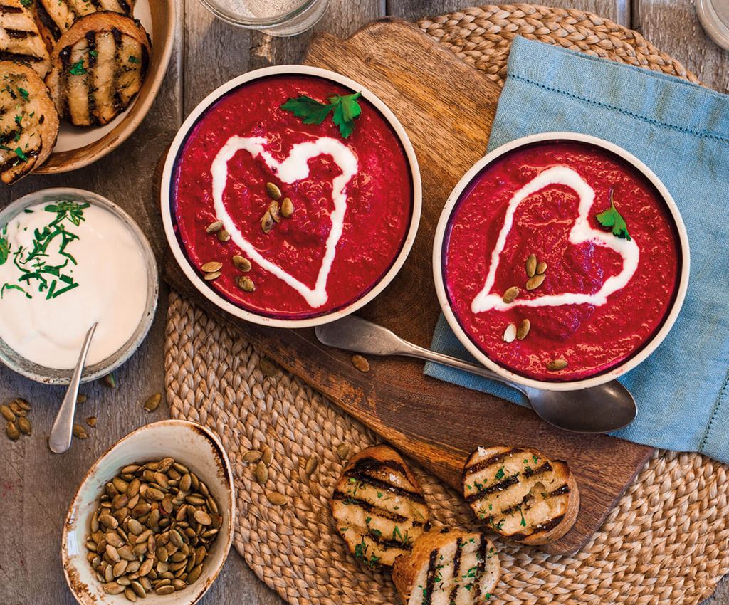 Two bowls of beetroot soup garnished with a heart of garlic yoghurt. Served with garlic bread