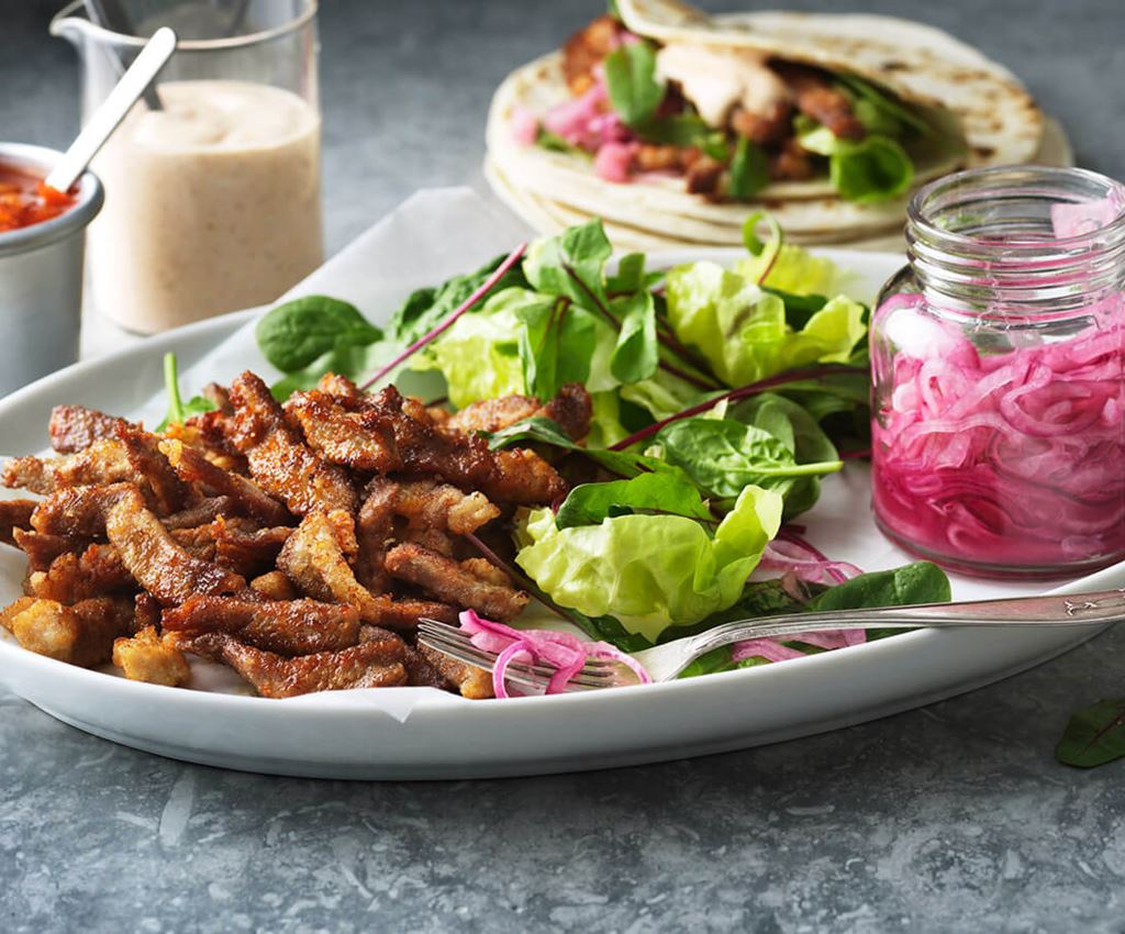 Chicharrónes on a plate with pickled red onions in a jar